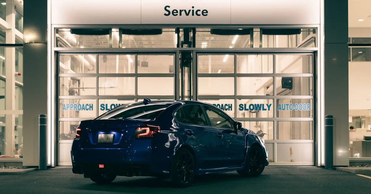Une voiture bleue élégante garée à l'entrée d'une station-service illuminée de nuit avec un éclairage moderne.