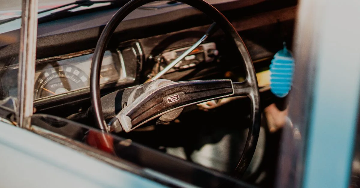 Gros plan sur l'intérieur d'une voiture vintage mettant en avant un volant classique et un tableau de bord.