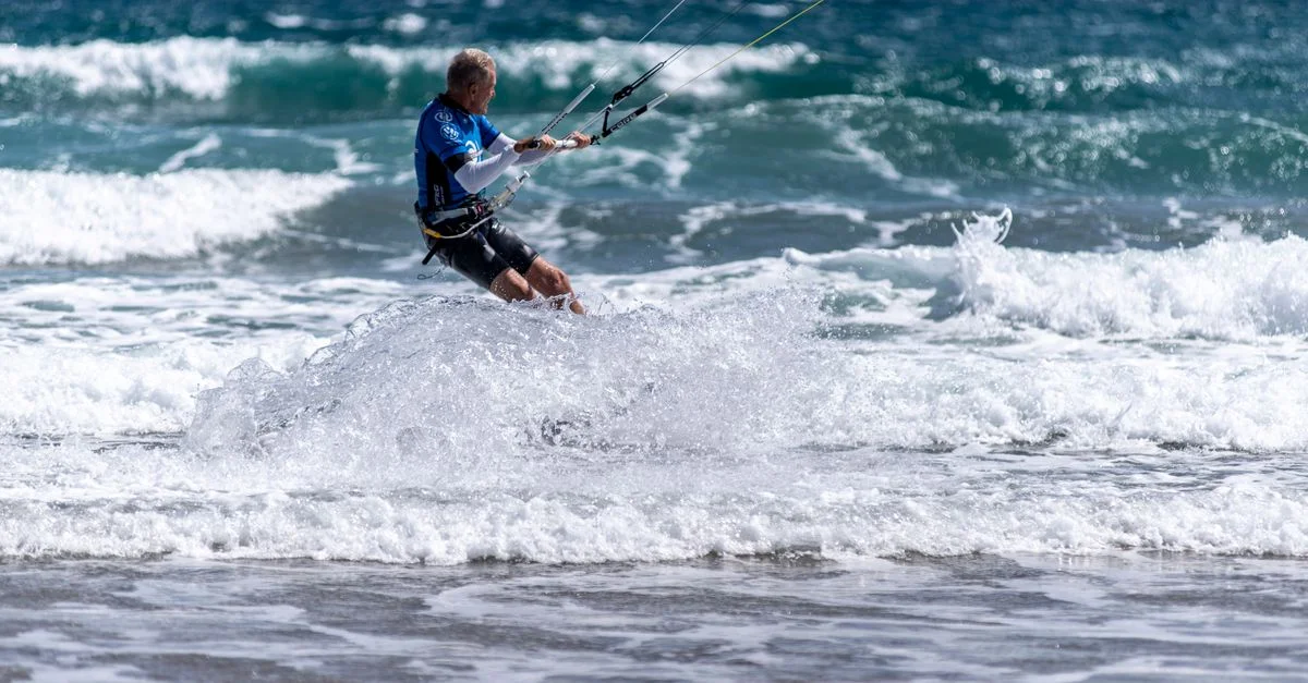 Scène de kitesurf exaltante avec des vagues s'écrasant sur une plage ensoleillée en Espagne.