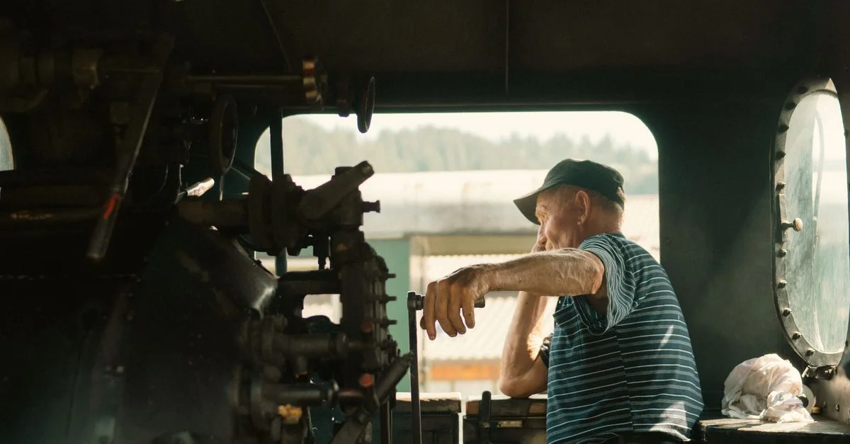 Un homme âgé contrôle une locomotive à vapeur vintage, capturant l'essence de l'ingénierie ferroviaire classique.