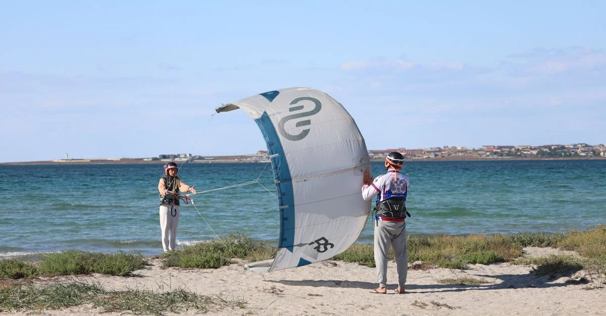 Deux personnes apprenant le kitesurf sur une plage ensoleillée avec un ciel bleu clair et une mer.
