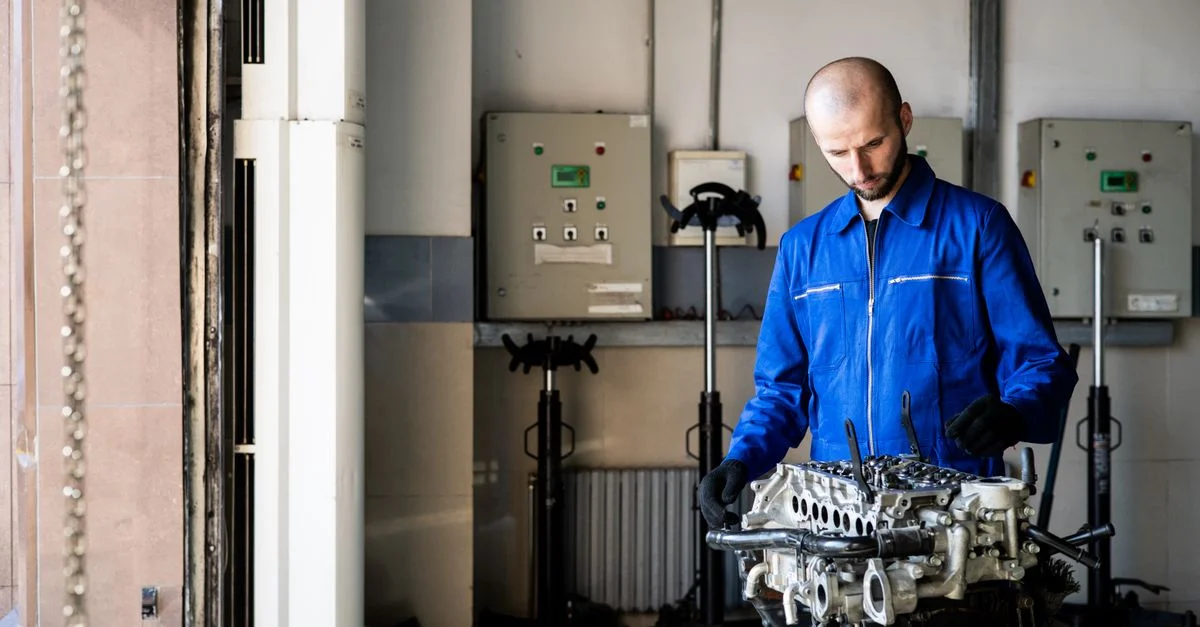 Un mécanicien en bleu de travail inspecte un moteur dans un atelier de réparation.