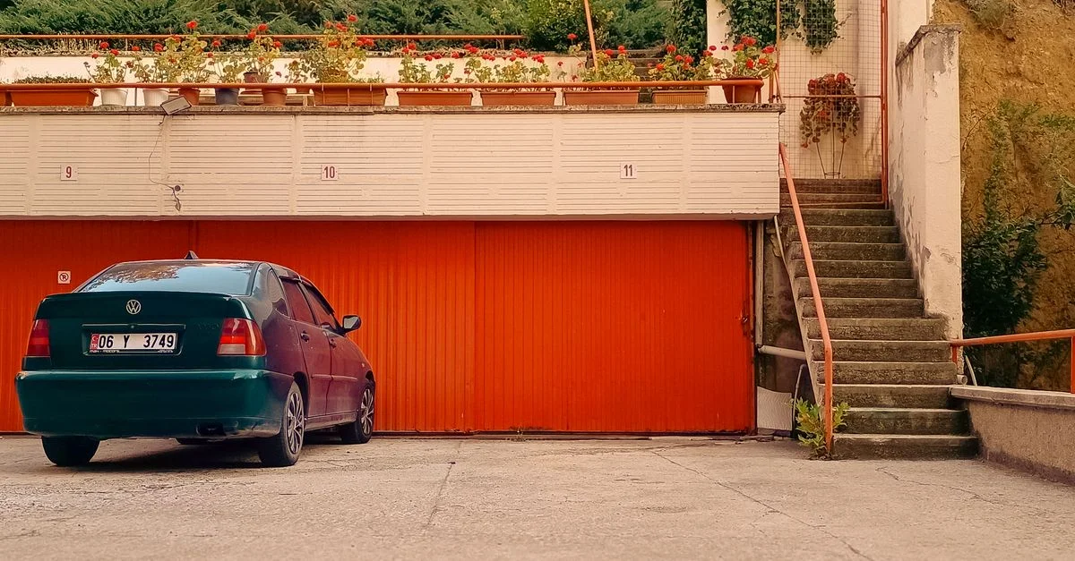 Une voiture verte garée devant des portes de garage orange vif, avec des plantes au-dessus.