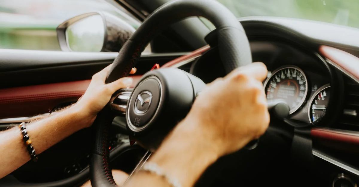 Gros plan des mains agrippant le volant d'une voiture avec des jauges de tableau de bord visibles.