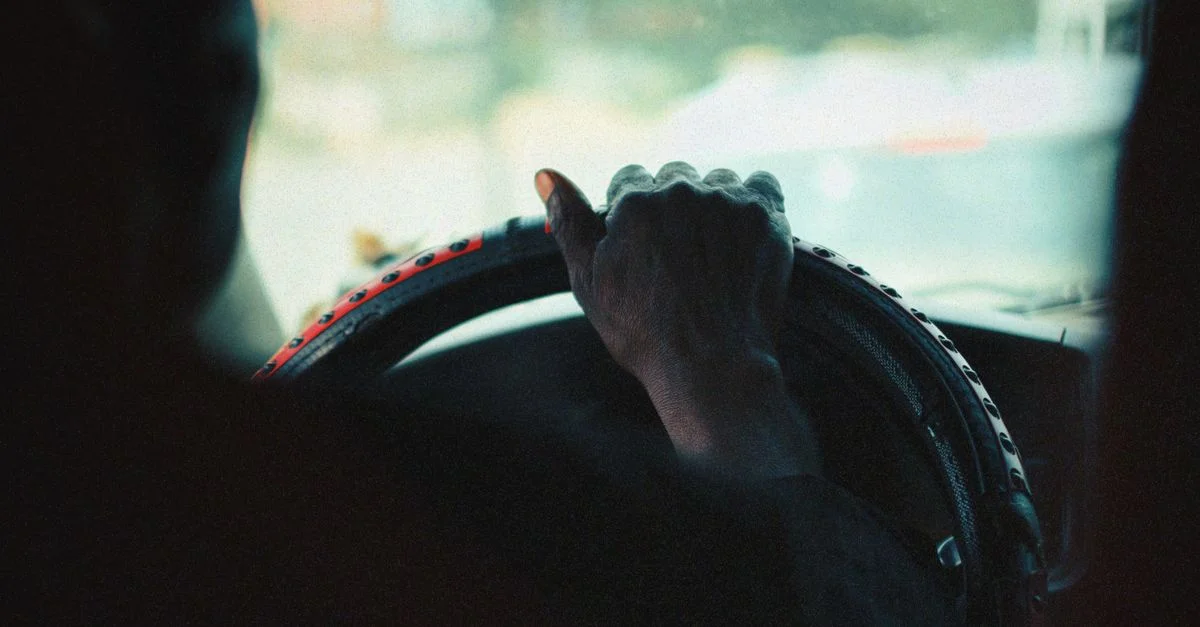 Gros plan sur la main d'une personne agrippant un volant de voiture, capturé dans un style vintage.