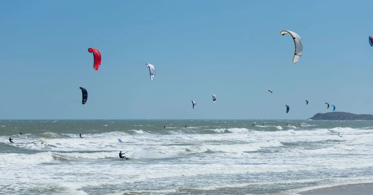 Des kitesurfeurs profitent d'une journée ensoleillée à la plage, surfant sur les vagues et planant dans la brise.